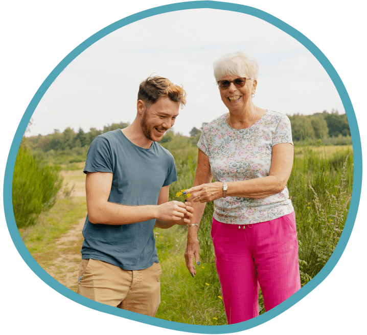 Male carer and female client looking at picked flowers on a park walk together