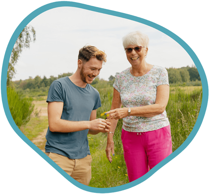 Male carer and female client looking at picked flowers on a park walk together
