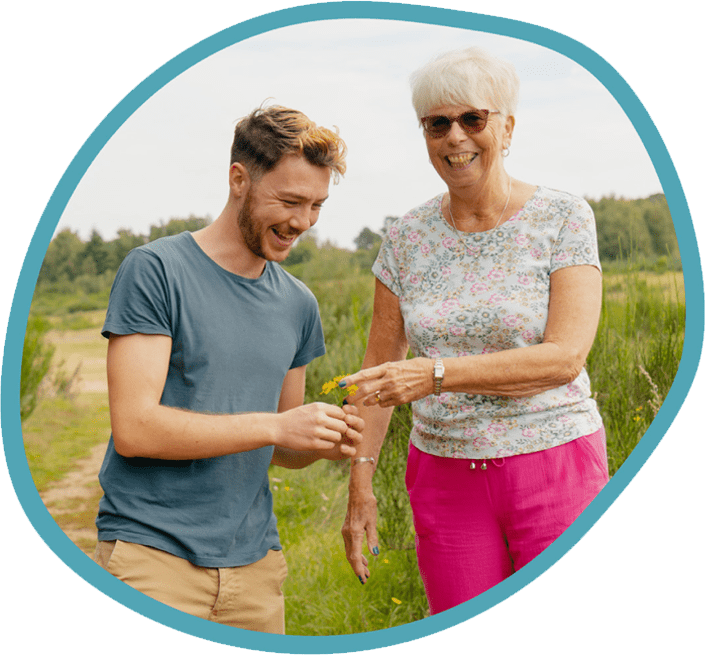 Male carer and female client looking at picked flowers on a park walk together
